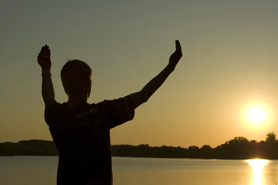 Mann holder opp hendene i solnedgang
