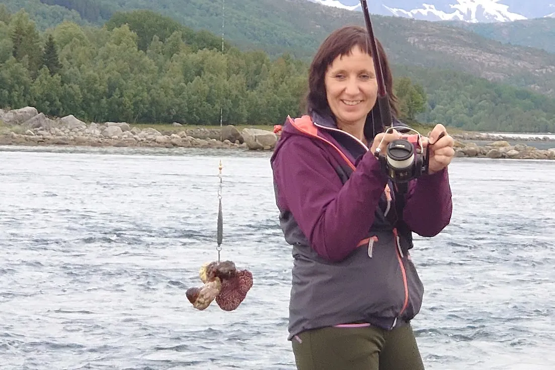 En kvinne som holder et kamera og en fisk i en innsjø